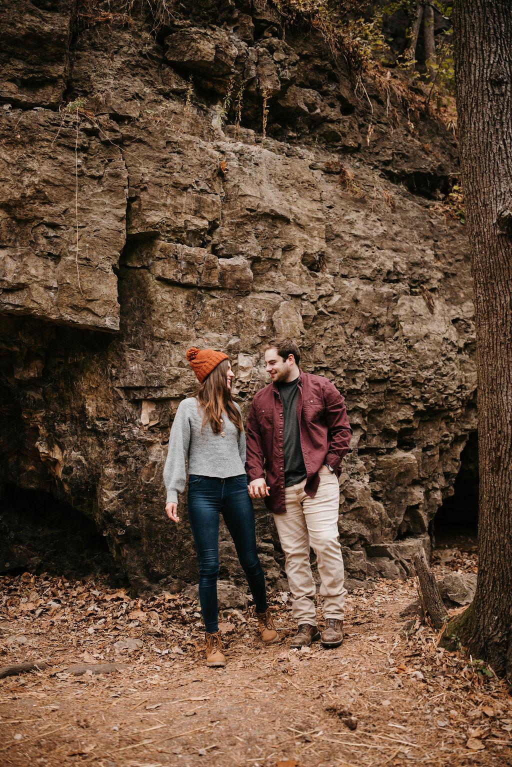 Morgan and Garrett are holding hands and smiling at each other in front of a cliff. Morgan is wearing an orange beanie.