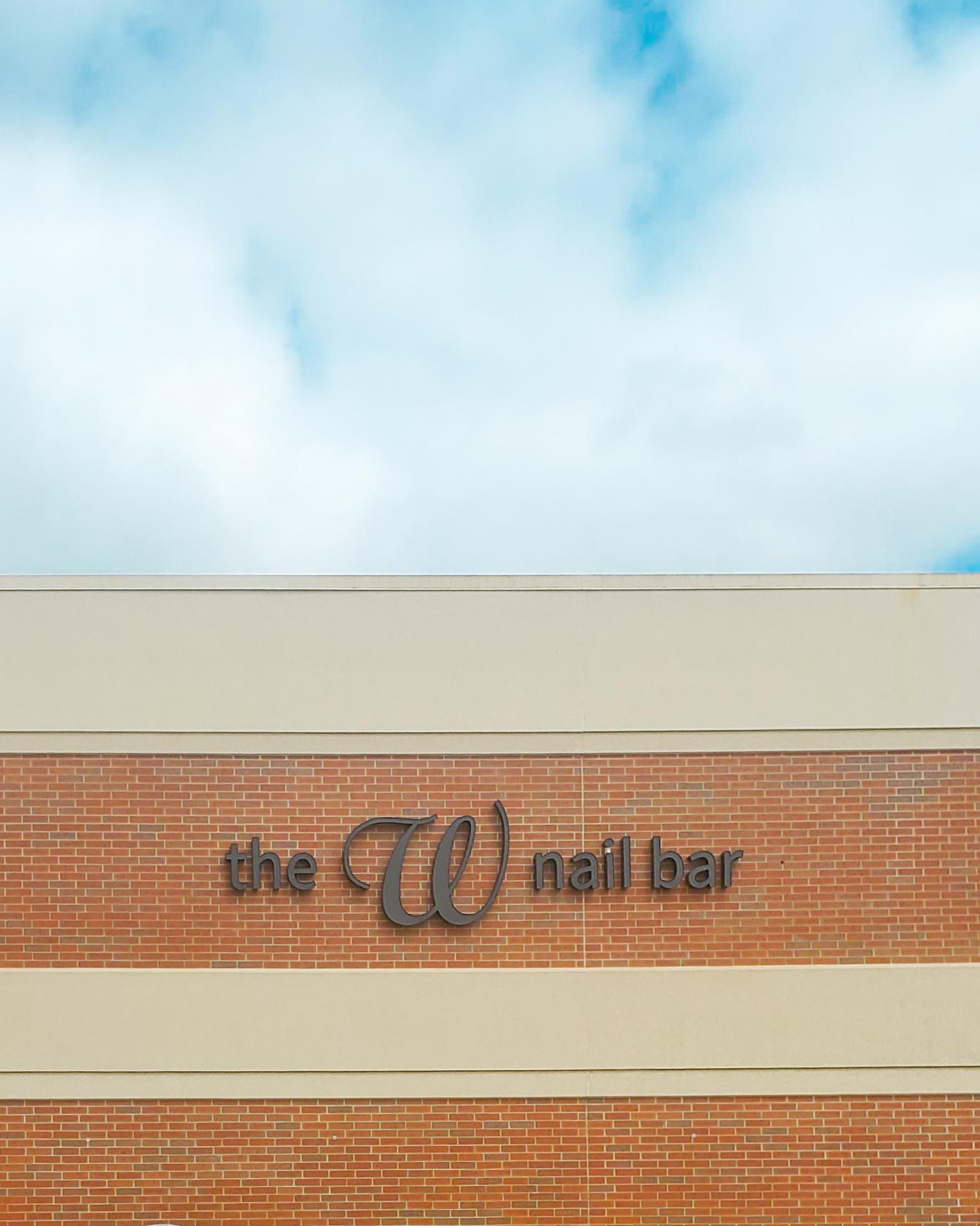 The W Nail Bar sign on the outside of the Quad Cities Hy-Vee in Bettendorf, Iowa. Above the sign are blue skies with a scattering of clouds.